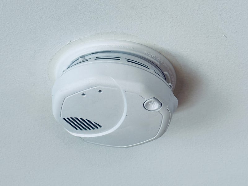 Une photo en gros plan d'un détecteur de fumée monté au plafond avec de la fumée blanche et un voyant rouge
