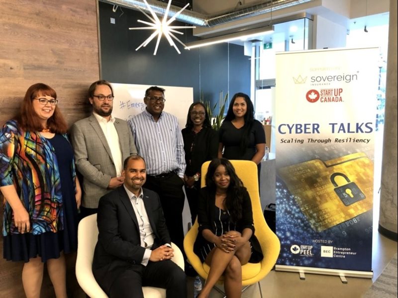 A group of people standing and sitting next to a pop up banner that reads "Cyber Talks scaling through resiliency"